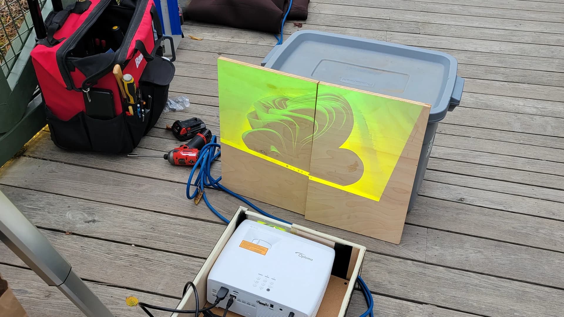 Outdoor daytime test setup showing a custom projector enclosure and dual test panels positioned on the boardwalk.